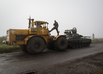 Un soldado ucraniano descansa y fuma sobre un tractor mientras remolca un tanque ruso capturado cerca de Izium, en la región de Kharkiv, en septiembre de 2022. La imagen del tractor arrastrando blindados rusos se convirtió en un meme viral y en símbolo del fracaso del plan inicial del Kremlin (REUTERS/Gleb Garanich)