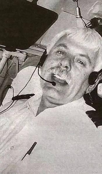 Fotografía en blanco y negro de un hombre con bigote y auriculares de aviación sentado dentro de la cabina de una aeronave