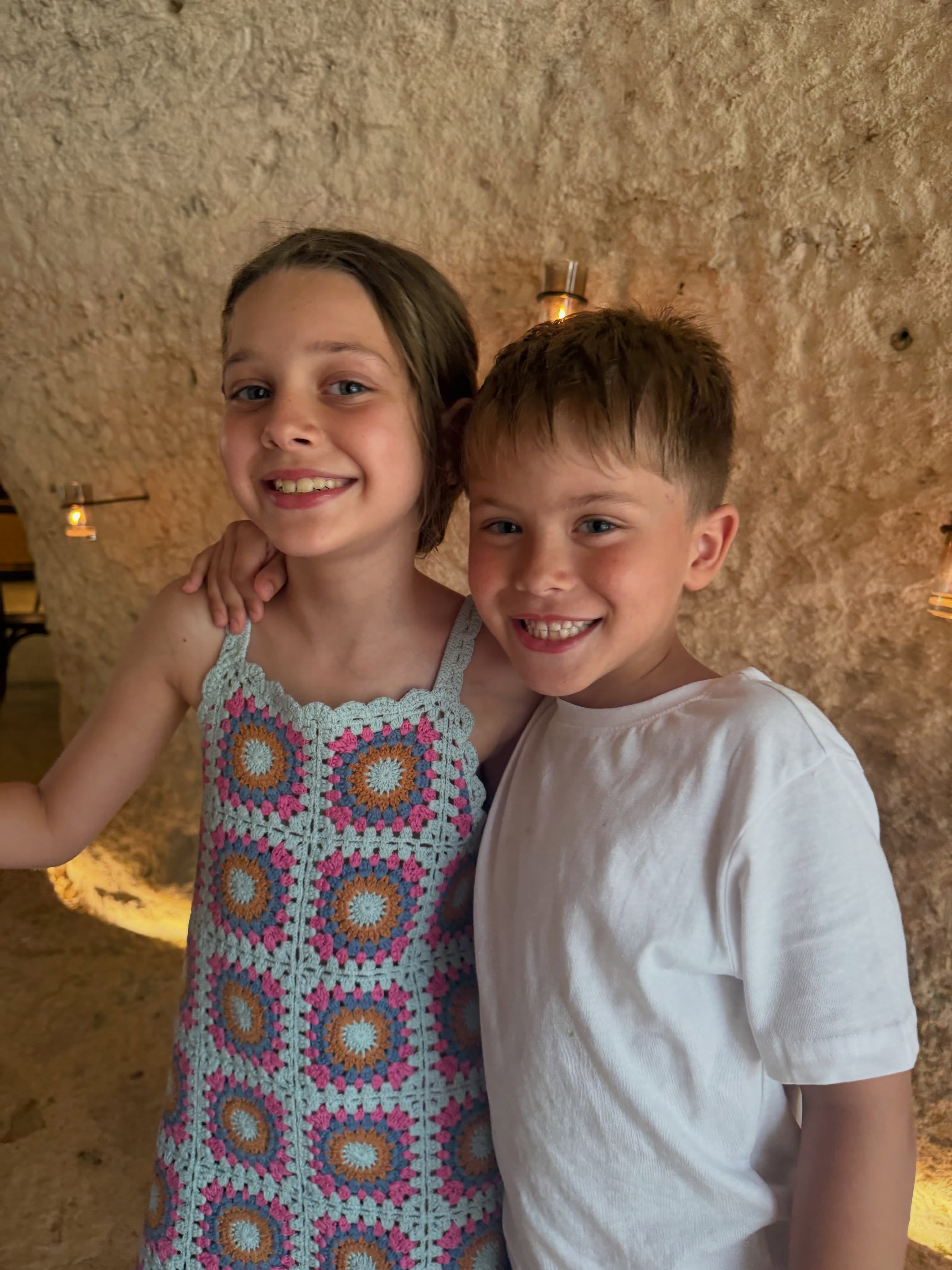 Los hijos de China Suárez posan sonrientes y abrazados frente a una pared de piedra iluminada durante un viaje de vacaciones