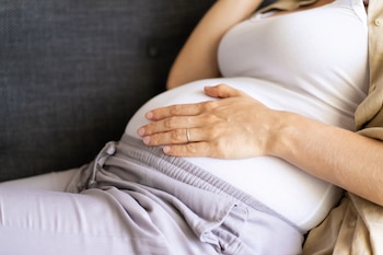 Una mujer embarazada se toca la barriga en el sofá de casa (Magnific)