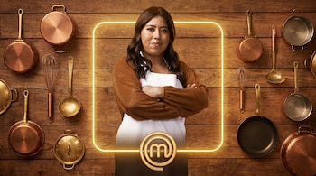 Mujer de pie con delantal blanco y brazos cruzados, enmarcada por un contorno luminoso, con el logo de MasterChef y utensilios de cocina sobre fondo de madera.