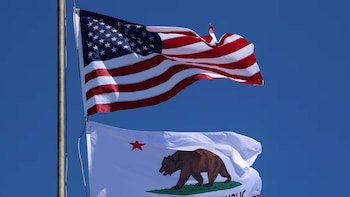 La bandera de Estados Unidos ondea por encima de la bandera de California, que muestra un oso pardo y una estrella roja, contra un cielo azul claro