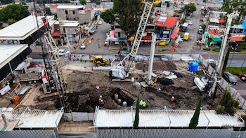 Vista aérea de un terreno en obra con grúas, una retroexcavadora, perforaciones en la tierra, columnas y obreros con cascos