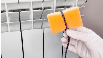 una mano con una esponja amarilla lista para limpiar los accesos más difíciles del radiador
