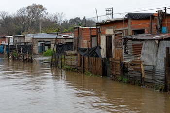 Viviendas precarias de ladrillo y chapa bordeadas por agua acumulada que cubre la calle en un asentamiento con postes de luz al fondo.
