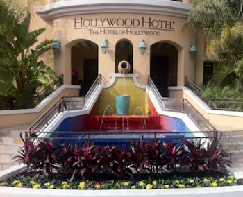 Fachada del Hollywood Hotel con su letrero. Incluye una fuente escalonada con azulejos amarillos, rojos y azules, flanqueada por escaleras y plantas