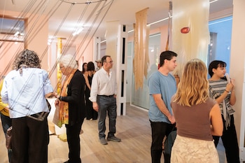 Grupo de personas en una galería, observando instalaciones de arte colgantes hechas de material translúcido y orgánico. El espacio tiene paredes claras e iluminación moderna