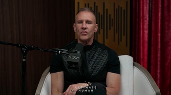 Un hombre sentado en un sillón blanco habla frente a un micrófono con el logotipo The Ultimate Human en un estudio