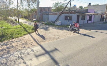 Una mujer camina por una calle de tierra junto a un repartidor en motocicleta con una caja roja en la parte trasera