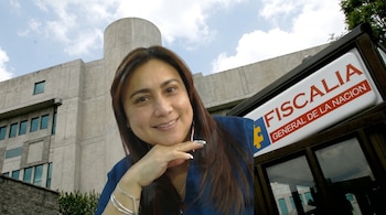 Yulixa Toloza sonriendo, con cabello castaño y blusa azul, posa frente a un edificio de concreto de la Fiscalía General y un letrero institucional.