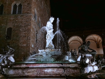 Estatua de mármol de Neptuno con agua en la Fuente de Neptuno, Florencia, iluminada de noche, con figuras de bronce y un edificio histórico de fondo