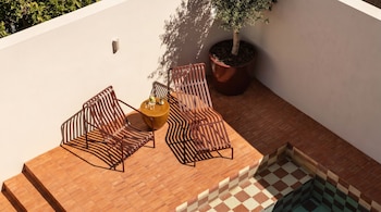 Patio exterior moderno visto desde arriba con dos sillas de metal marrón, mesa amarilla, planta en maceta, suelo de terracota y una pequeña piscina con azulejos a cuadros.