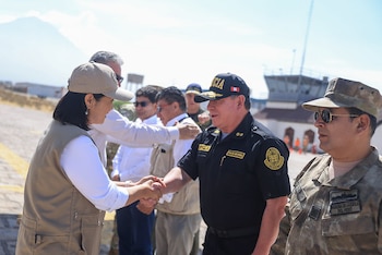 Una mujer con gorra saluda con un apretón de manos a un policía en un aeródromo en presencia de oficiales militares y civiles