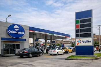 Estación de servicio en Lima con surtidores, varios coches y taxis, edificios urbanos y carteles con los logos de Osinergmin y Facilito.