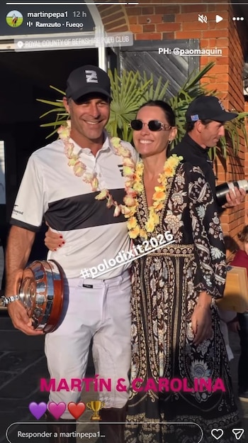 Hombre y mujer sonrientes con collares de flores posan juntos al aire libre. El hombre, a la izquierda, sostiene un trofeo y viste ropa de polo. La mujer lo abraza