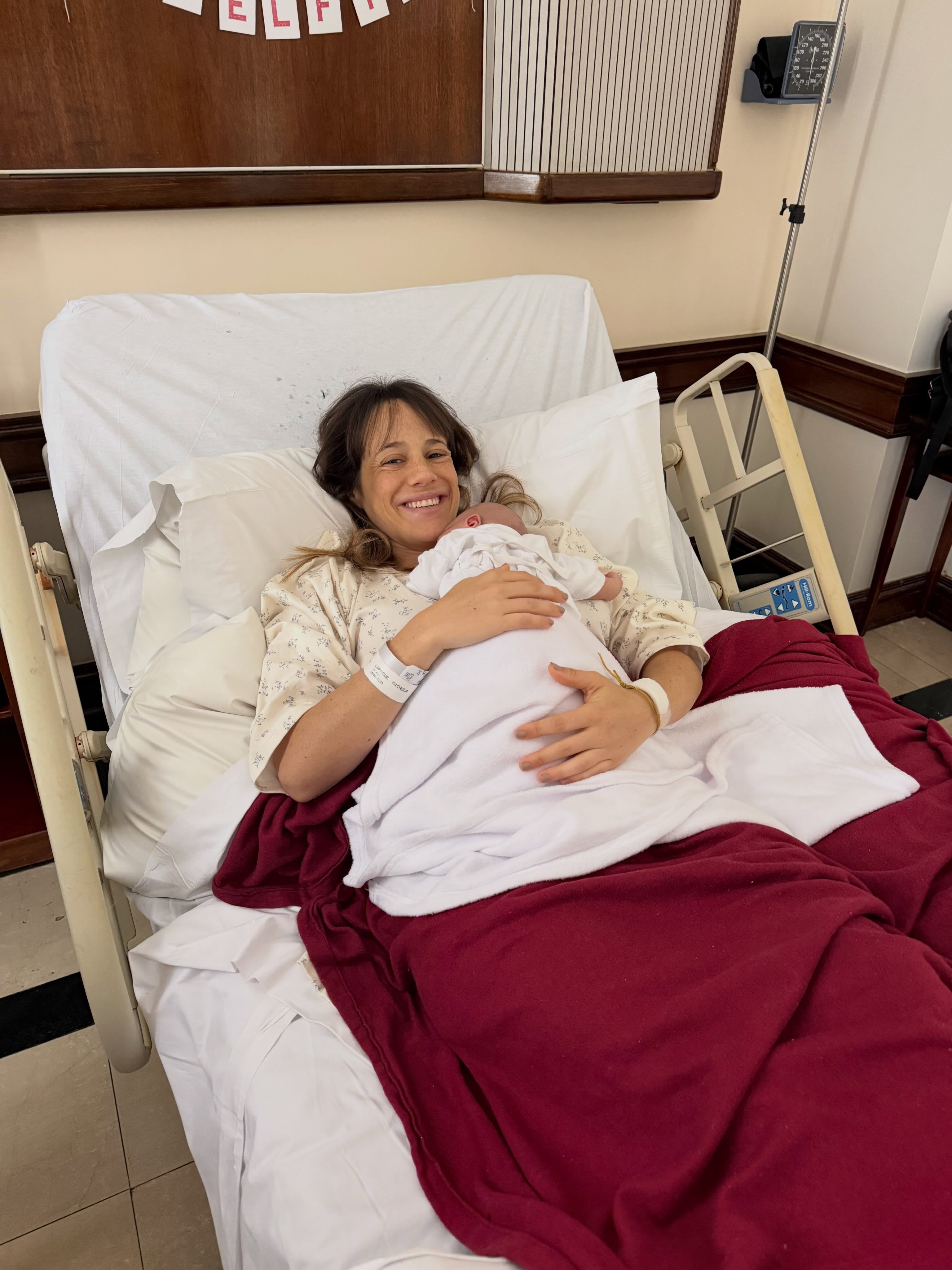 Mica descansa en una cama de hospital mientras sostiene en brazos a su hija recién nacida.