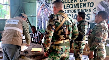 Un hombre con chaleco de Sucamec revisa folios sobre una mesa de madera junto a tres personas con uniforme militar camuflado.