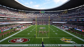 Vista del campo de fútbol americano en el Estadio Azteca con los escudos de los 49ers y Vikings pintados en las zonas de anotación.