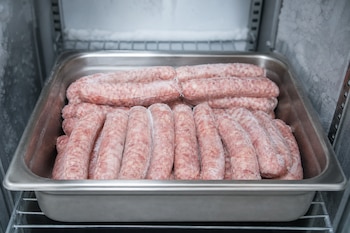 Salchichas de cerdo crudas cubiertas de escarcha colocadas sobre una bandeja metálica dentro de un congelador.