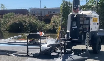 Un generador móvil, barreras flotantes de contención en el agua, una silla plegable negra y lonas junto a un cuerpo de agua