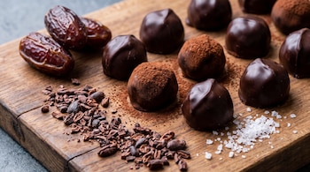 Bombones de chocolate, dátiles enteros, trozos de cacao y granos de sal sobre una tabla de madera.