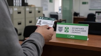 Mano sosteniendo una Licencia Permanente CDMX. En el fondo, un letrero de la Secretaría de Movilidad (Semovi) y el interior desenfocado de una oficina.