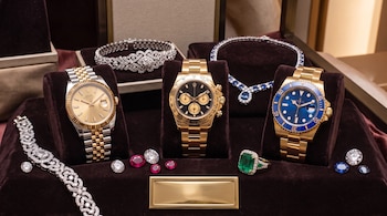 Tres relojes de pulsera, pulseras de diamantes, un collar, un anillo de esmeralda y gemas sueltas sobre soportes de terciopelo oscuro.