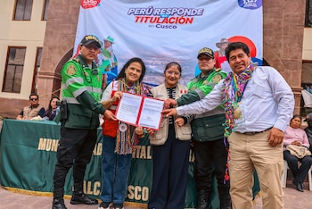 Dos policías, dos mujeres y un hombre sostienen una carpeta abierta con un documento frente a un cartel institucional y una mesa