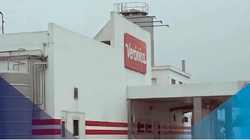Fachada blanca de un edificio industrial con el logo rojo 'Verónica'. Se observan tuberías metálicas, franjas rojas y azules en la parte inferior de la imagen