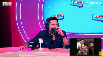 Hombre con auriculares y micrófono en un estudio con luces de neón, un teléfono, una taza y una pantalla con la imagen de tres hombres