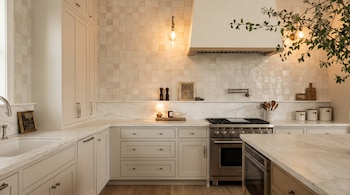 Cocina con gabinetes y encimeras de mármol, salpicadero de azulejos, estufa con horno, campana extractora, fregadero y elementos decorativos.