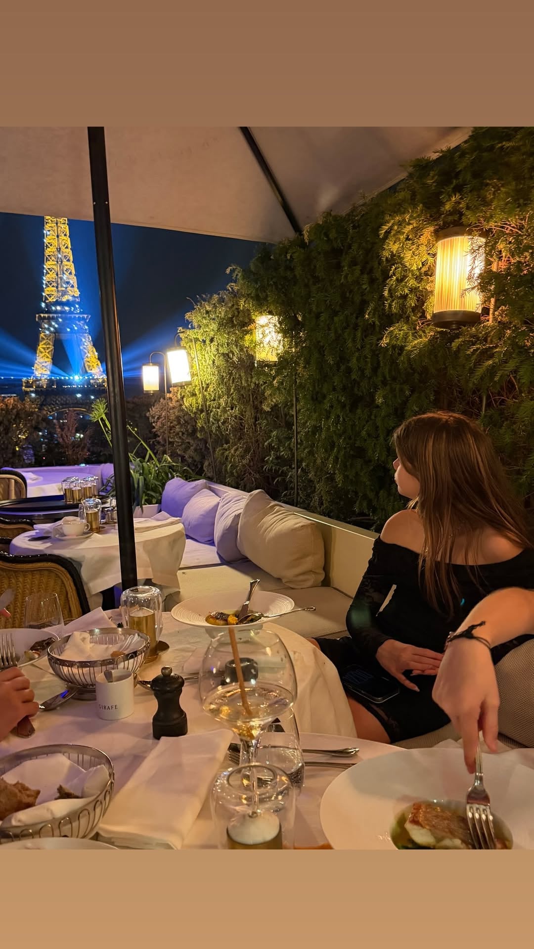 Una de las hijas de Wanda, de espaldas y con vestido negro off-shoulder, observa la Torre Eiffel iluminada desde la terraza del restaurante Girafe