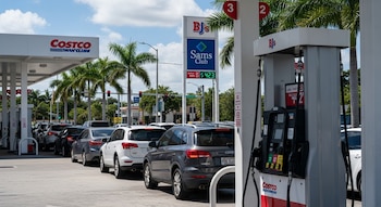 Estación de servicio Costco en Miami con fila de autos esperando combustible. Un surtidor muestra el precio del galón a USD 4,42. Palmeras y cielo azul.