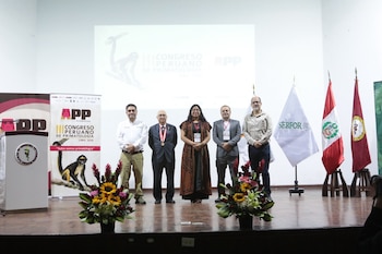 Cinco personas en un escenario con un podio, tres banderas y una pantalla de proyección con texto 'III Congreso Peruano de Primatología Lima, 2026'