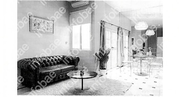 Sala de estar con sofá capitoné, mesa de centro, alfombra, ventana, planta de interior y un juego de comedor con sillas