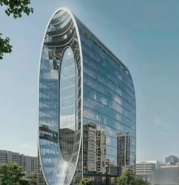 Un moderno edificio de vidrio y metal de 14 pisos con una forma ovalada distintiva, que refleja el cielo azul y otros edificios circundantes