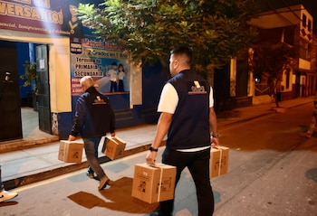 Miembros del personal de la Oficina Nacional de Procesos Electorales (ONPE) trasladan cajas con materiales electorales por una calle urbana durante la noche, como parte de la organización de comicios.