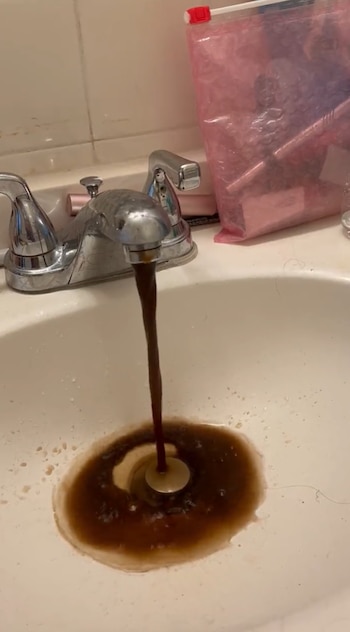 Agua de color marrón oscuro sale de un grifo metálico y cae en un lavabo blanco