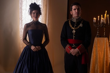 Un hombre con uniforme militar de gala y una mujer con vestido largo azul oscuro y un velo negro con lunares. Detrás, un candelabro con velas