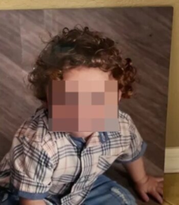 Un niño pequeño con cabello rizado castaño y camisa a cuadros, con la cara pixelada