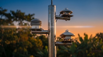 Estructura metálica de medición meteorológica con sensores y piranómetros sobre un fondo de vegetación al atardecer.