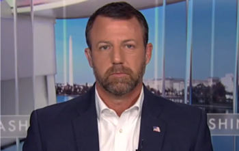 Foto de Markwayne Mullin, um homem caucasiano com barba e cabelos escuros, vestindo terno azul marinho e camisa branca. Ao fundo, vagamente, você pode ver um monumento semelhante ao Monumento a Washington