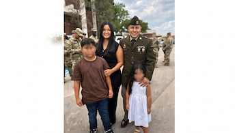 Un hombre con uniforme militar, una mujer de negro y dos niños con rostros borrosos posan junto a otros soldados en el exterior.