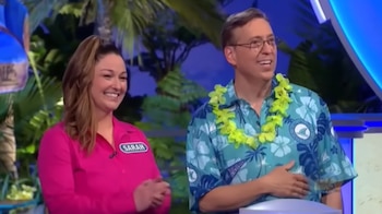 Un hombre con camisa hawaiana verde y guirnalda de flores sonríe junto a una mujer vestida de rosa que aplaude en un plató de televisión