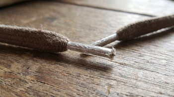 Dos extremos de un cordón de tela marrón con puntas de plástico transparente sobre una mesa de madera.