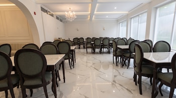 Un salón comedor interior con mesas de madera, sillas con tapiz verde, suelo de mármol blanco y una araña de cristal en el techo.