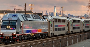 Locomotora eléctrica plateada de NJ Transit, número 4539, en vías. Detrás, el horizonte de Nueva York con rascacielos al atardecer