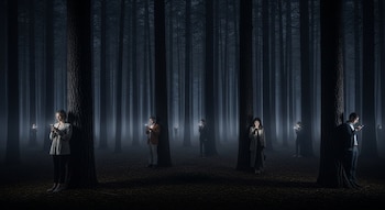 Bosque denso y oscuro con árboles altos y niebla; varias personas de pie, vestidas, cada una mirando y sosteniendo un teléfono celular encendido.