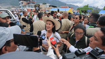 Una mujer con sombrero de paja rodeada por periodistas con micrófonos y cámaras en una vía pública