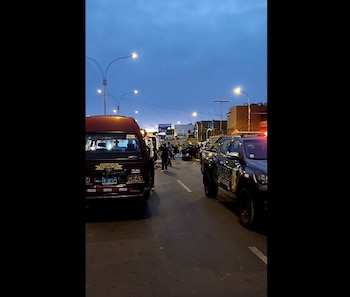 Una cúster de transporte público y un vehículo policial permanecen en una avenida con alumbrado público al atardecer